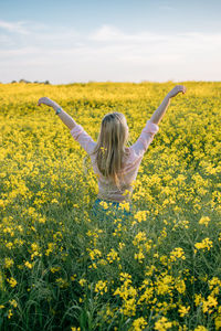 Rear view of young woman with yellow flowers in field