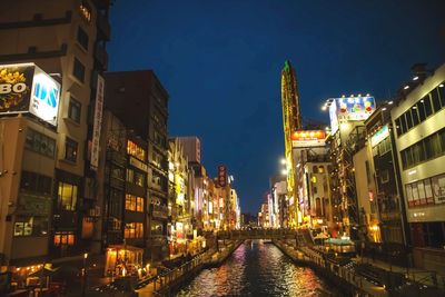 Illuminated street amidst buildings against sky at night. 