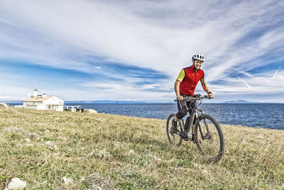 Full length of mountain biker on field against sea