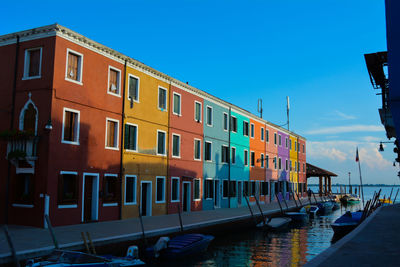 Boats moored in canal by buildings against sky