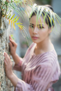 Portrait of young woman by wall and plants