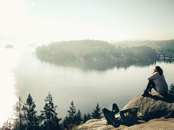 Man sitting by lake against sky