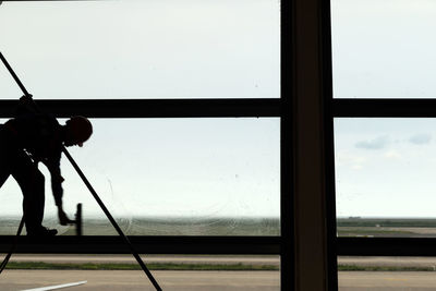 Silhouette man working in glass window against clear sky