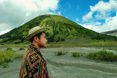 Side view of young man looking away while standing against mountain