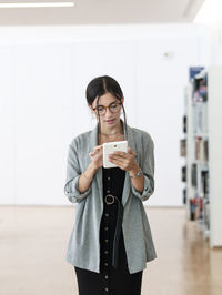 Female in glasses using tablet while standing in spacious workplace and working on project