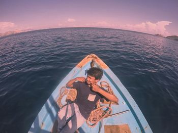 High angle view of young man looking away while sitting in boat on sea against sky during sunset