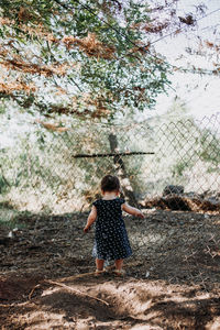 Rear view of girl standing by chainlink fence on field