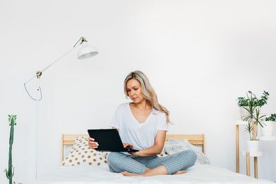 Young woman using mobile phone while sitting on bed