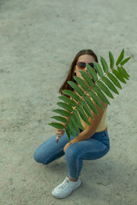 Portrait of young woman in sunglasses holding plant outdoors