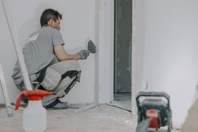 A young builder is plastering a doorway.
