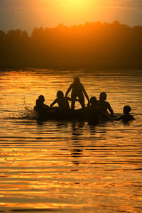 Silhouette people in sea against sky during sunset