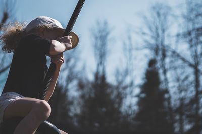 Low angle view of girl swinging on tire swing against sky