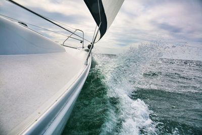 Water splashing by sailboat sailing on sea against sky