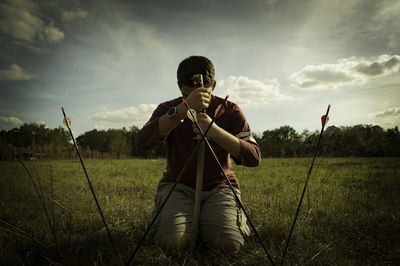 Man kneeling by arrows on field against sky