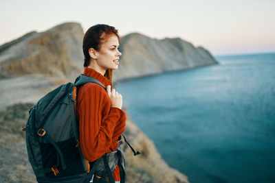 Woman standing on rock by sea against sky