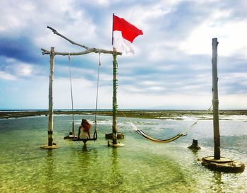 Rear view of woman sitting on swing in sea against sky