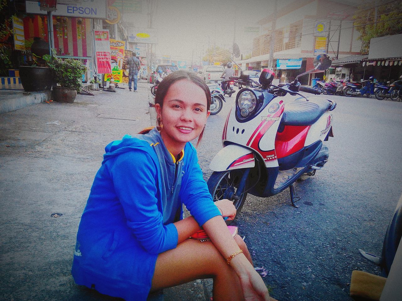 PORTRAIT OF A SMILING YOUNG WOMAN SITTING ON STREET