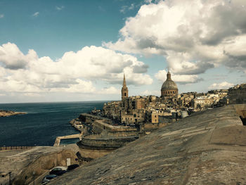 Buildings in town by sea against sky