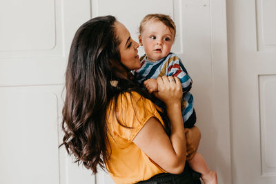 Mother carrying son while standing by door at home