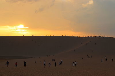 People at beach against sky during sunset