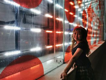 Portrait of young woman looking at illuminated glass at night