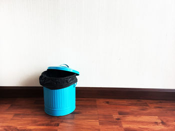 Garbage can on wooden floor against wall