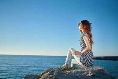 Side view of young woman against sea against clear sky