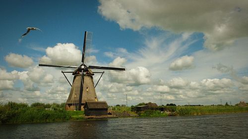 Low angle view of traditional windmill by river against sky