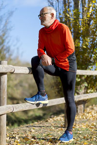 Thoughtful senior man looking away while standing by wooden railing at park