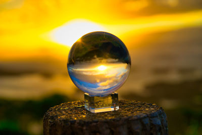 Close-up of crystal ball on wooden post at sunset