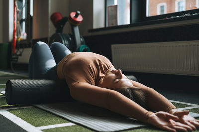 Young brunette woman doing stretching pilates on massage roll in the fitness club gym