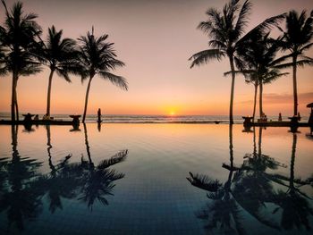 Silhouette palm trees by swimming pool against sky during sunset