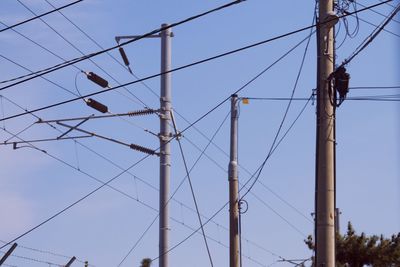 Low angle view of electricity pylons against blue sky