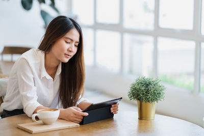 Young woman using mobile phone while sitting on table