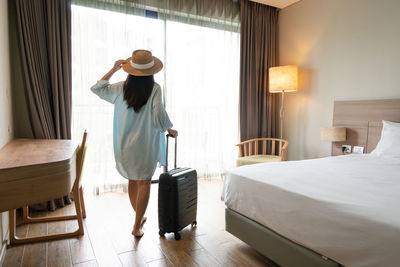 Rear view of woman sitting on bed at home