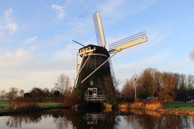 Traditional windmill by lake against sky