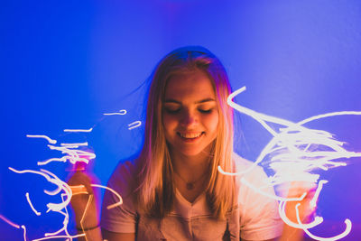 Close-up of smiling young woman amidst light painting against blue background