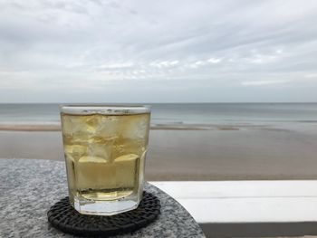 Glass of water on beach against sky