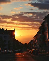 Cars on road by buildings against sky during sunset