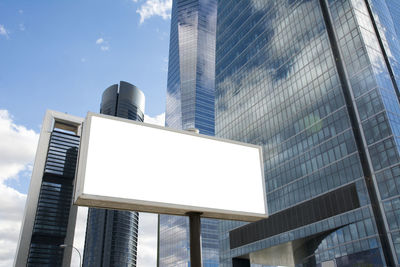 Low angle view of blank billboard against modern buildings in city