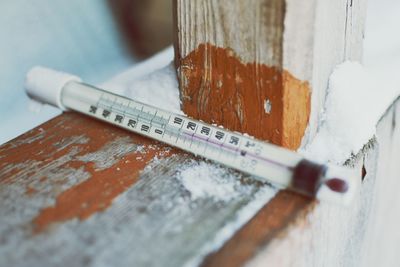 Close-up of thermometer on wooden railing during winter