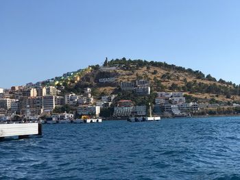 Buildings by sea against clear blue sky