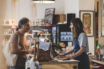 Female sales clerk talking with customer at checkout counter in deli