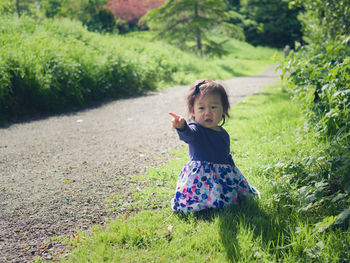 Girl pointing while kneeling on grassy field by footpath