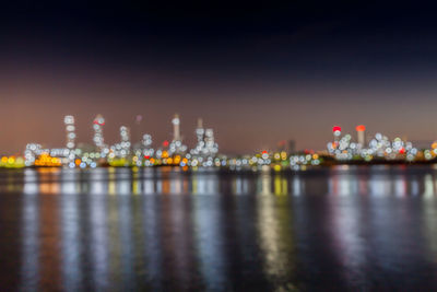 Illuminated city by sea against sky at night