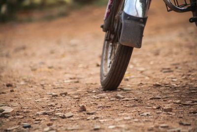 Low section of person riding motorcycle on dirt road