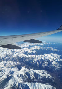 Airplane flying over snowcapped mountains against blue sky