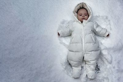 Directly above shot of cute baby lying on snow covered field during winter