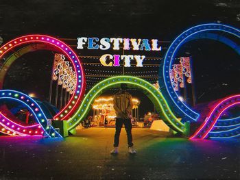 Rear view of woman standing against illuminated lights at night