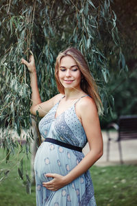 Smiling pregnant woman standing by tree branches on field